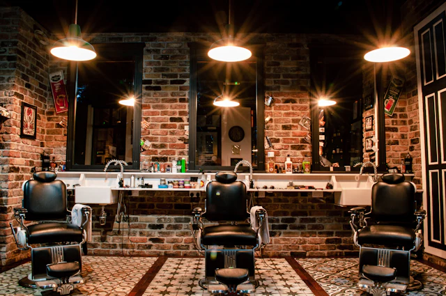 Salão da barbearia com cadeiras de couro e parede de tijolos